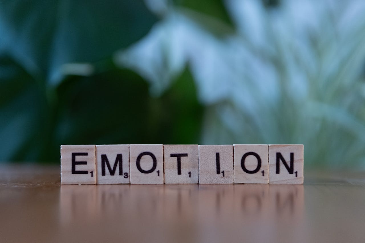 Wooden Scrabble tiles spelling 'Emotion' with a natural blurred background.