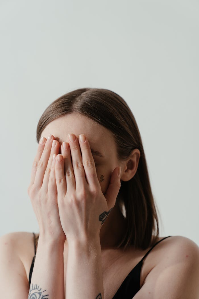 A woman covers her face with hands, exuding a sense of shyness and anonymity.
