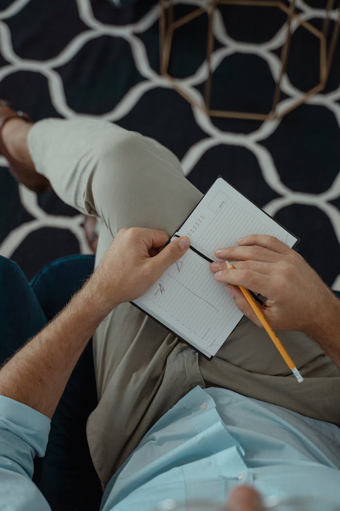 Overhead view of a man taking notes in a notebook with a pencil, sitting cross-legged indoors.